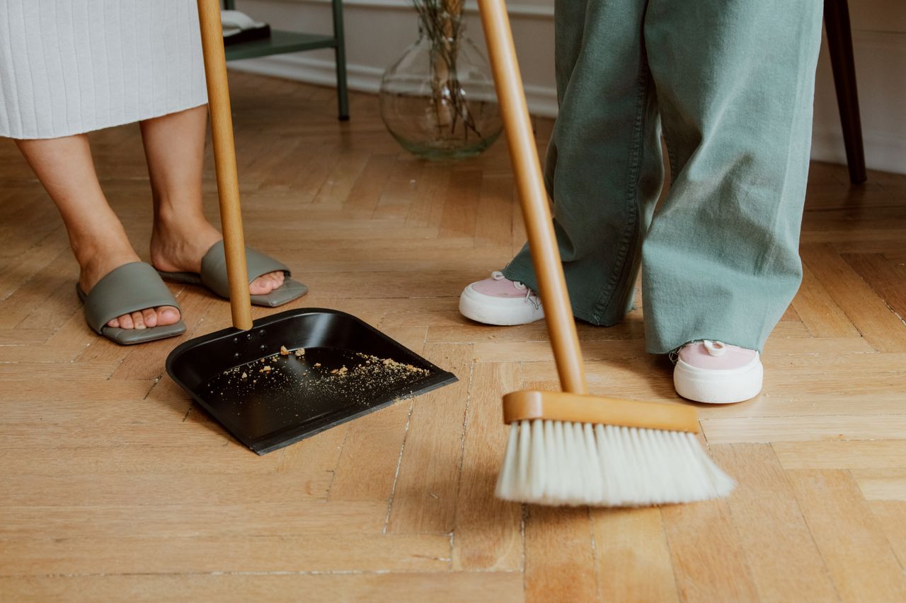 services-01 Gros plan sur des personnes nettoyant un sol en bois avec un balai et une pelle à poussière à l’intérieur.